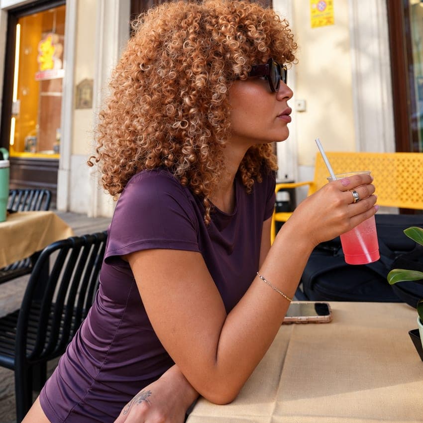 Una ragazza a un tavolino all'aperto sotto i portici, con la tovaglia e una bibita